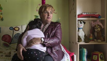 Justi Carretero, madre de acogida de una menor, que sostiene en sus brazos, en su dormitorio de Cabanillas del Campo.