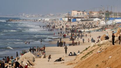 Cientos de palestinos aguardan en una playa de Gaza con la esperanza de recibir ayuda lanzada desde el aire.