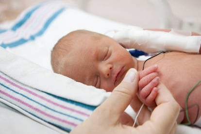 Una madre sostiene la mano de un bebé en una incubadora.