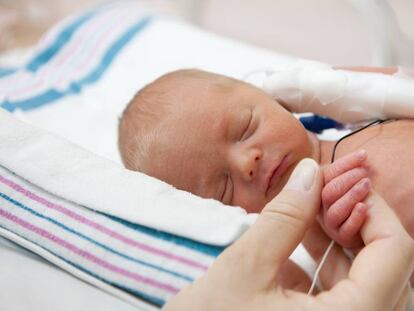Una madre sostiene la mano de un bebé en una incubadora.