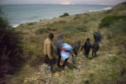 El camino desciende hacia la playa. La luz que se aprecia al fondo probablemente corresponde a Gibraltar. Es el último tramo antes de los momentos de máxima tensión. El grupo lleva un guía, que es quien les conduce hasta la playa y les va dando instrucciones. Cada uno de los integrantes del grupo tiene un móvil que está apagado y ha guardado en el interior de un preservativo. Es la manera más segura para protegerlo del agua. El guía será quien avise a Salvamento Marítimo de España de la presencia de una embarcación, cuando ésta ya esté en el mar.