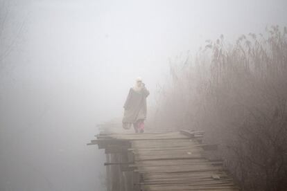 Una mujer musulmana camina por un puente en el lago Dal, en una fría mañana con niebla en Cachemira.