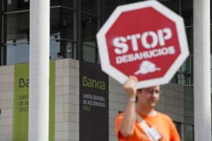 Un hombre sujeta un cartel en protesta por los deshaucios a las afueras del Palacio de Congresos de Valencia donde está teniendo lugar, esta mañana, la primera junta de accionistas de Bankia a menos de un mes del primer aniversario de su debut en Bolsa y con el enfado de miles de clientes e inversores, que se sienten engañados por el descalabro de la acción.