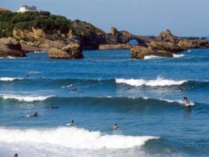 Surfistas disfrutan de las olas de Biarritz. Al fondo, la Roca de la Virgen, un paseo costero muy concurrido.