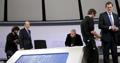 Técnicos de sonido colocan los micrófonos a Rubalcaba y Rajoy.