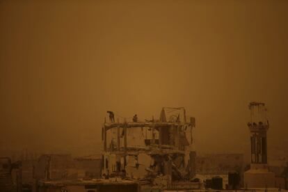 Obreros palestinos trabajan retirando los escombros de un edificio en la ciudad de Gaza durante una tormenta de arena.