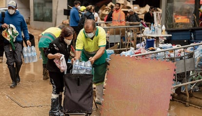 Un hombre carga agua en el carro de una mujer en las puertas del Auditorio de Paiporta.