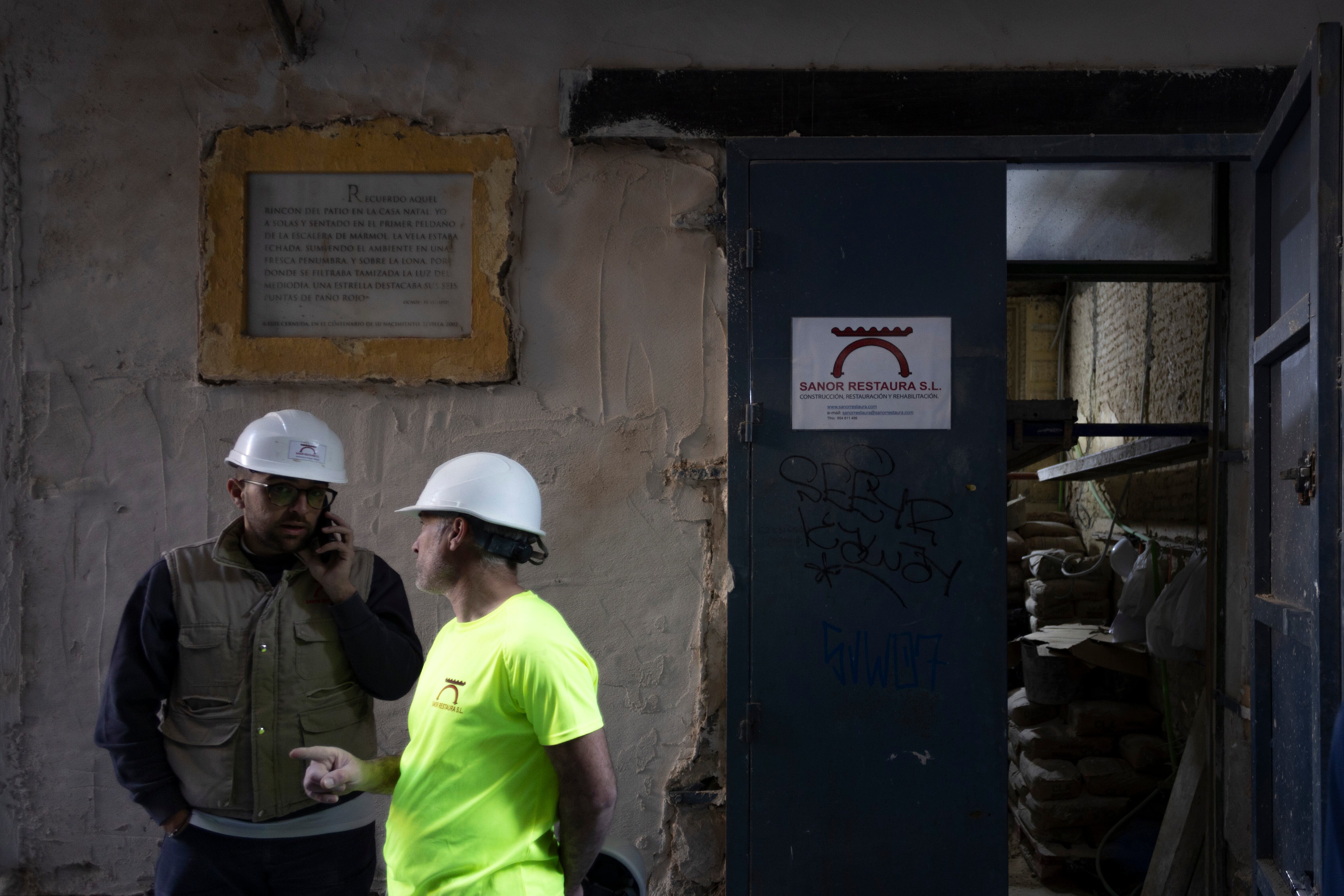 Dos operarios frente a placa informativa en el exterior de la vivienda indicando que fue la casa de Luis Cernuda.