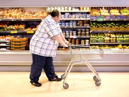 Un hombre obeso pasa delante de comida saludable en un supermercado.