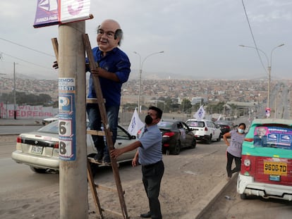 Un hombre con una máscara de Hernando de Soto coloca un cartel antes de una aparición del candidato en Villa El Salvador, Lima, el pasado 5 de abril.