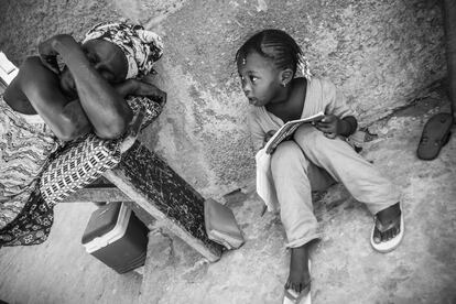 Una niña lee un cuento en el patio de su casa mientras su abuela descansa después de cocinar para toda la familia en el barrio de pescadores de Yoff (Senegal), año 2012. Aquí las mujeres son quienes realizan trabajos dentro y fuera de casa. La tasa de escolarización de niños y niñas es muy desigual en Senegal: según los datos del Banco Mundial, en 2015 el 36,2% de las niñas solo trabajaban y no iban al colegio, aunque poco a poco se va avanzando en igualdad de derechos.