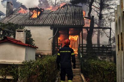 Un bombero junto a una casa incendiada en Kineta (Grecia).