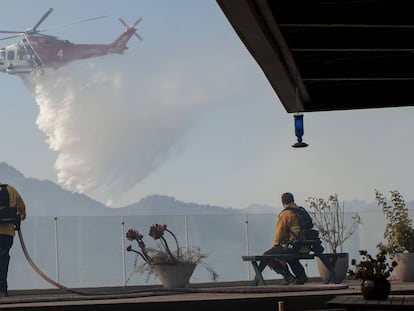 Los bomberos observan cómo un helicóptero arroja agua en un incendio forestal en el área de Pacific Palisades de Los Ángeles.