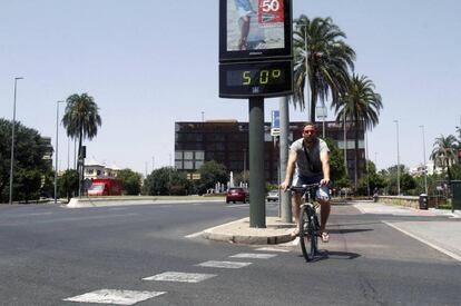 Un joven pasa con su bicicleta junto a un termómetro que marca 50 grados en Córdoba.