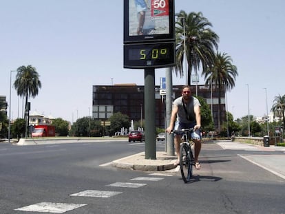 Un joven pasa con su bicicleta junto a un termómetro que marca 50 grados en Córdoba.