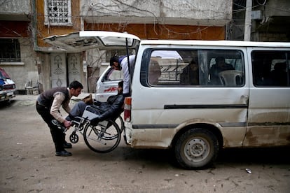 Mohamed Barkhash, de 25 años, con una lesión de médula espinal, es ayudado por otros hombres a subir al autobús que transporta a los pacientes al centro de rehabilitación de Douma, en Damasco (Siria).