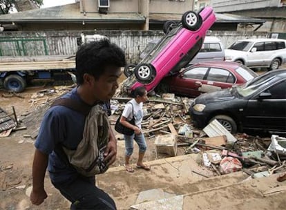 Ciudadanos filipinos pasan al lado de coches dañados por las inundaciones en la ciudad de Marikina.