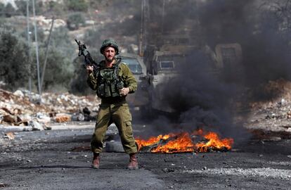 Un soldado israelí sujeta su arma cerca de unos neumáticos ardiendo durante los enfrentamientos con palestinos en el asentamiento judío de Qadomem cerca de Nablus, West Bank.