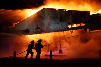 Muchos de los edificios en llamas han quedado destruidos. Los vándalos han aprovechado el caos para saquear algunos comercios. En la foto, los bomberos intentan apagar el fuego en un establecimiento comercial.