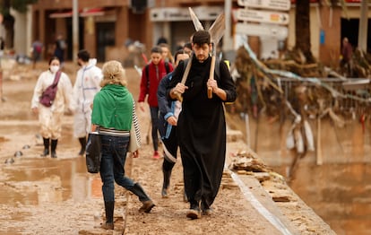 Un sacerdote con dos palas camina entre el barro de una calle de Paiporta (Valencia) afectada por la dana, este lunes.