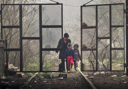 Una mujer migrante y dos ni?os caminan a travs de la puerta de un hangar donde han establecido sus tiendas de campa?a en la frontera griega de Idomeni.