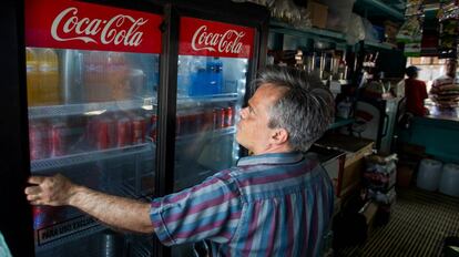 Un hombre cierra un refrigerador con latas de Coca Cola.