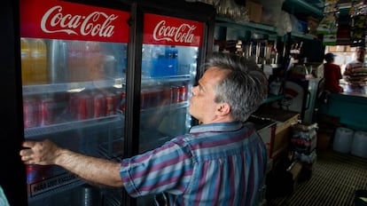 Un hombre cierra un refrigerador con latas de Coca Cola.