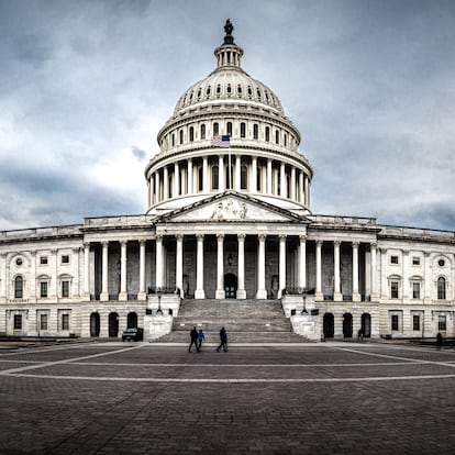 Panoramic view of rear facade of Capitol building in Washington, D.C. on a cloudy and moody day. Some tourist passing in front of it.