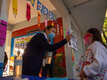 Una maestra toma la temperatura de una estudiante antes de ingresar al salón de clases.