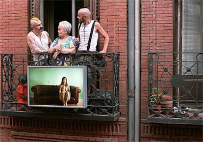 El artista Alexis W. (a la derecha) charla con unos vecinos de Chueca detrás de una de las obras que expone en un balcón de la calle de Pelayo.