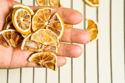 Una mano sostiene varias rodajas de limón liofilizado, sobre un fondo blanco.