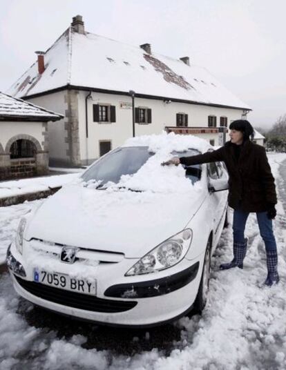 Una mujer limpia la nieve acumulada en su vehículo tras la nevada que ha caído en Navarra, en las zonas por encima de los 1.100 metros.