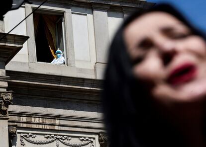 Una persona con un traje de protección mira desde una ventana mientras una cantante de ópera interpreta el primer acto de 'La Bohème' de Giacomo Puccini, en el exterior del teatro de La Scala como parte de una protesta contra la crisis del sector del entretenimiento causada por la pandemia de covid-19 y las restricciones, en Milán, Italia.