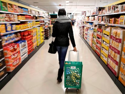 Una mujer carga su carrito de la compra por el pasillo de un supermercado.