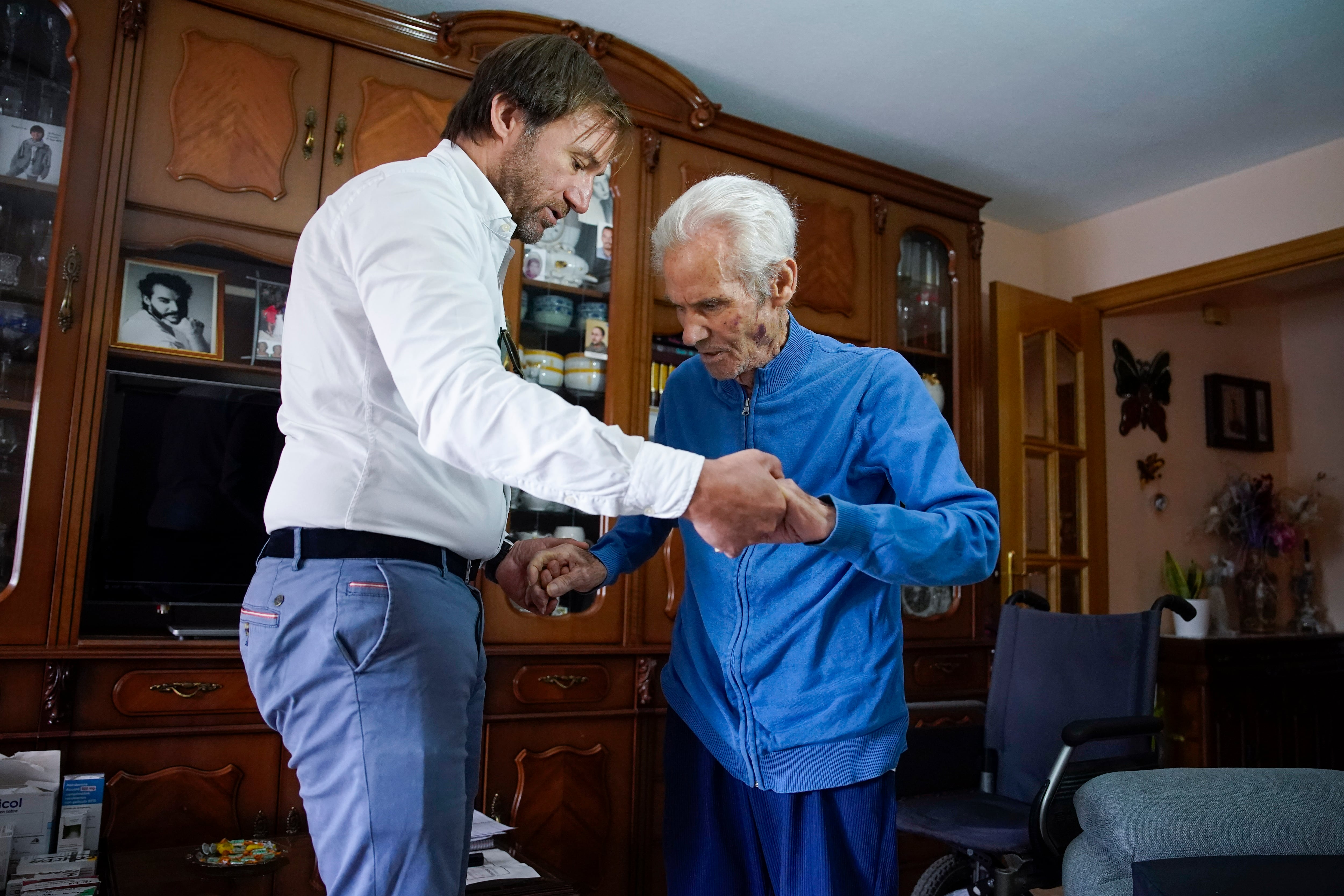El voluntario de paliativos David Mínguez, izquierda, ayuda a Domingo a sentarse en su casa de Madrid.