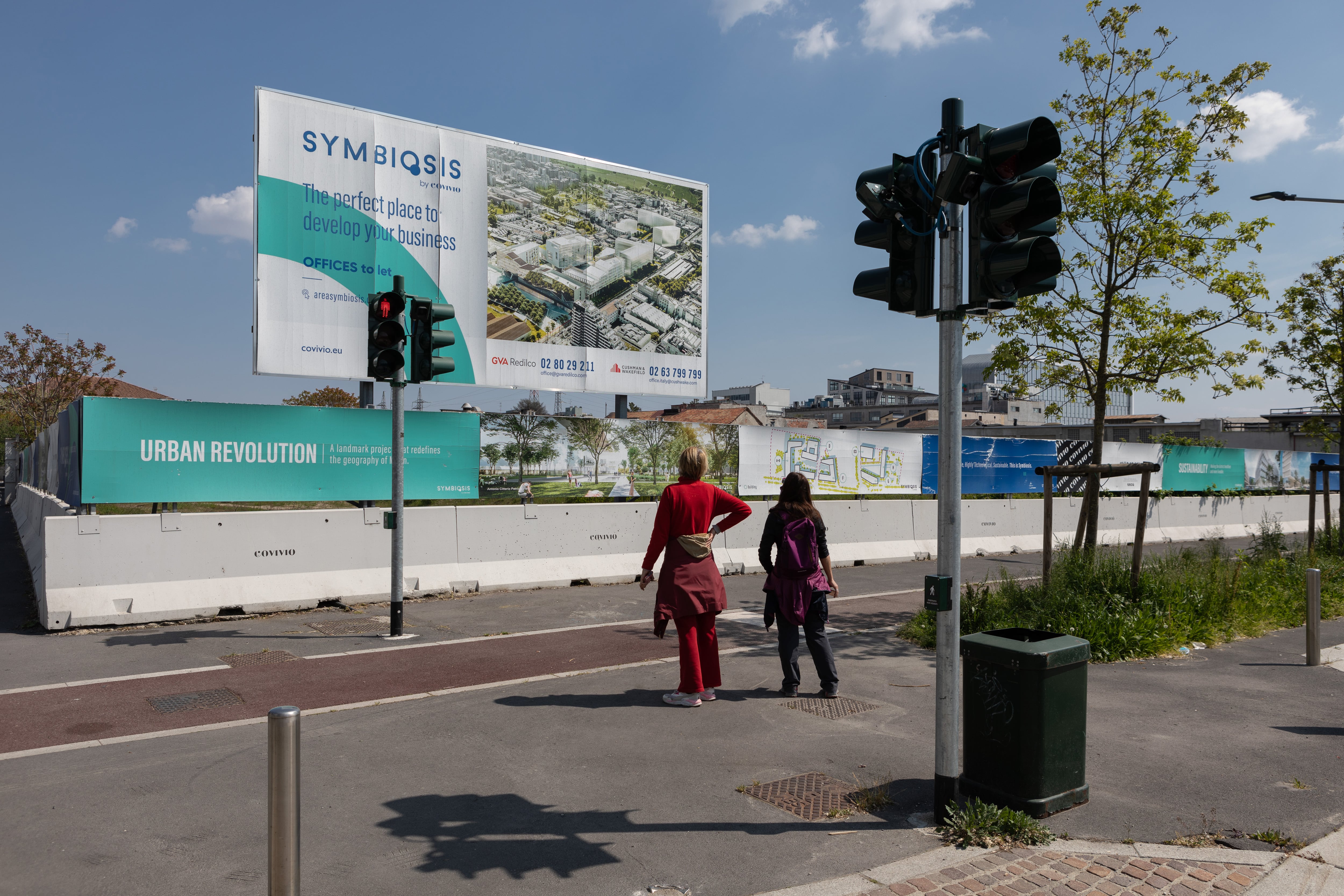 Dos mujeres miran una valla publicitaria que muestra una imagen generada por computadora del futuro distrito comercial de Symbiosis,  en Milán, Italia.