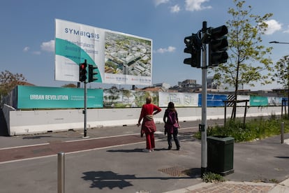 Dos mujeres miran una valla publicitaria que muestra una imagen generada por computadora del futuro distrito comercial de Symbiosis,  en Milán, Italia.