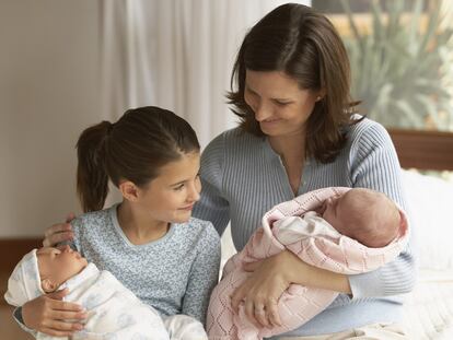 Imagen familiar en la que una niña con un muñeco imita el rol de su madre con el bebé.