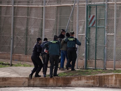 Agentes de la guardia civil preceden a expulsar por la valla a dos migrantes que acababan de saltar la valla de Melilla, en 2014.