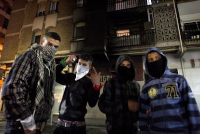 Youths with their faces covered on the streets of Salt in front of a building damaged by fire during the weekend's disturbances.