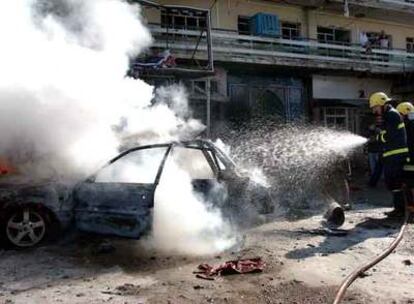 Dos bomberos se afanan por extinguir uno de los coches bomba que explotaron ayer en Kirkuk, al norte de Irak.
