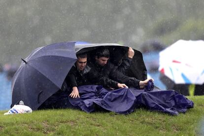 Tres aficionados tratan de cubrise de la lluvia en el circuito de Silverstone