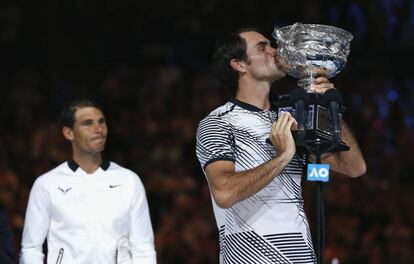 Roger Federer besa el trofeo del Open de Australia ante la mirada de Nadal.