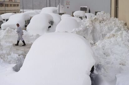 Una persona camina entre los coches cubiertos de nieve en Burguete (Navarra).