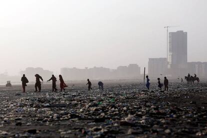 Mujeres y niños caminan a través de la basura dejada por las olas del mar a lo largo de la playa de Clifton en Karachi, Pakistán.