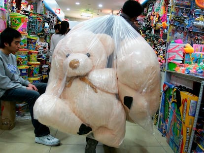 Un trabajador transporta osos de peluche dentro de una bolsa en una tienda durante la época navideña.