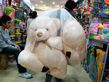 Un trabajador transporta osos de peluche dentro de una bolsa en una tienda durante la época navideña.