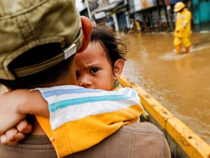 Un padre coge en brazos a su hija para cruzar las calles inundadas en Yakarta.