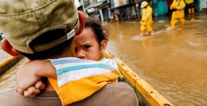 Un padre coge en brazos a su hija para cruzar las calles inundadas en Yakarta.