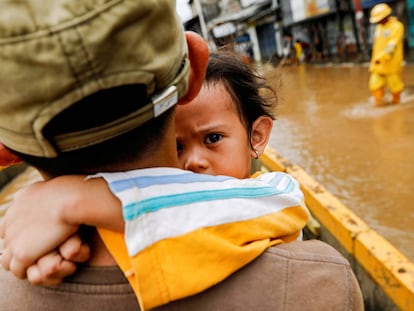 Un padre coge en brazos a su hija para cruzar las calles inundadas en Yakarta.